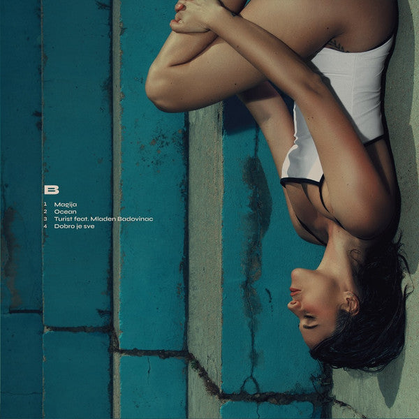Person hanging upside down against a blue wall with album tracklist.
