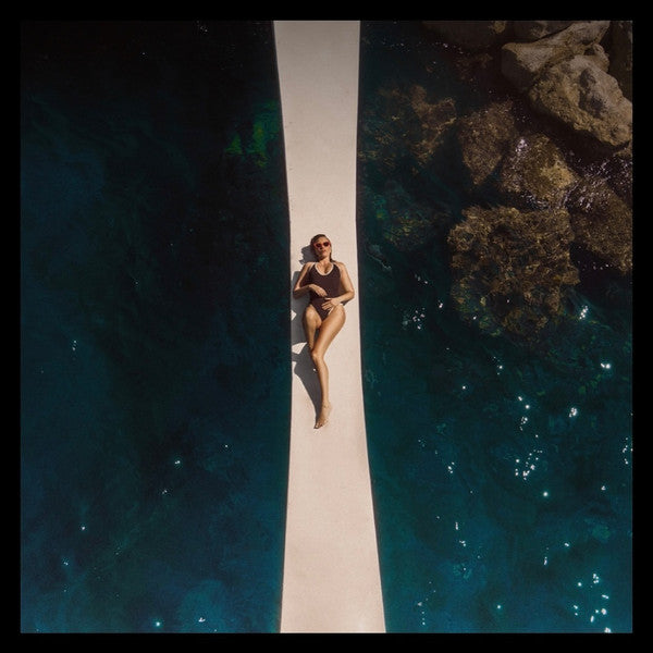 Person lying on a dock over crystal-clear blue water with a rocky island in the background