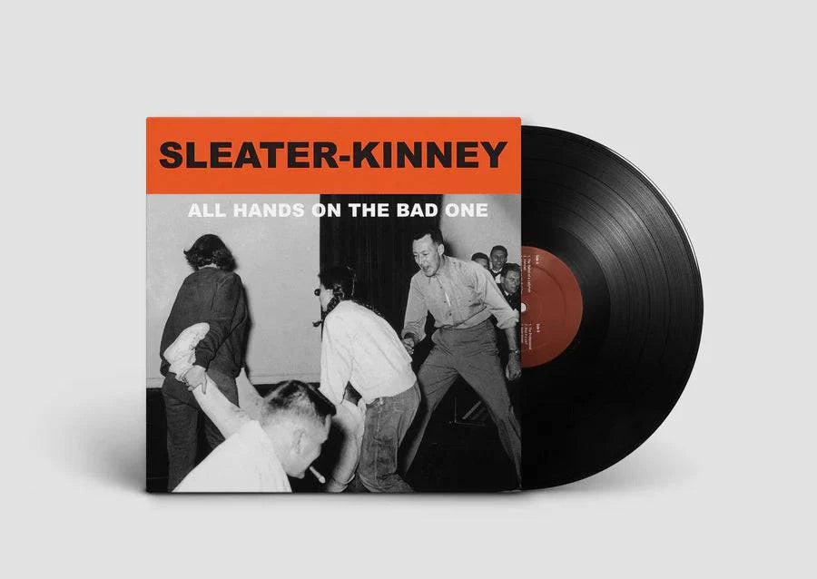Vinyl record with 'Sleater-Kinney' album cover showing a group of people in a room.