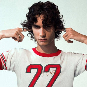 sombr album cover white young man with black curly hair in white t-shirt with red number 22 holding fingers in his ears 